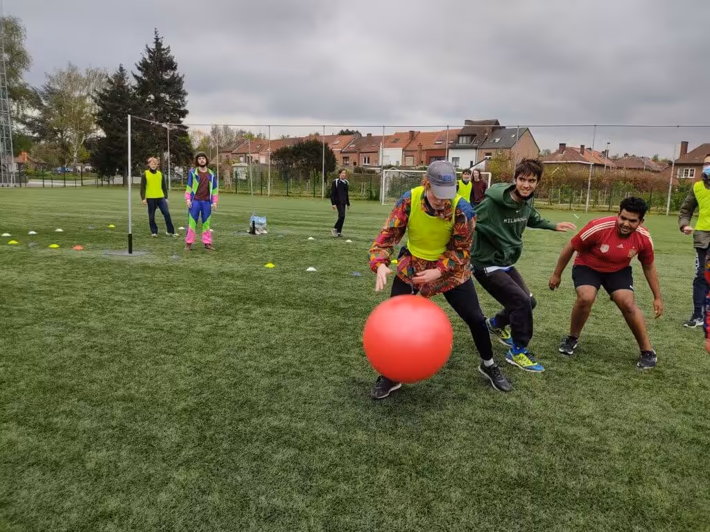 Mensen spelen met grote rode bal op grasveld.