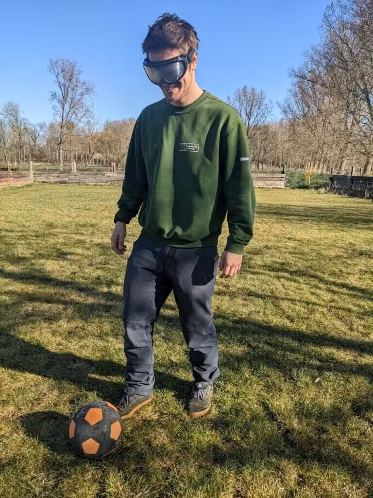 Man speelt voetbal met speciale bril op grasveld.