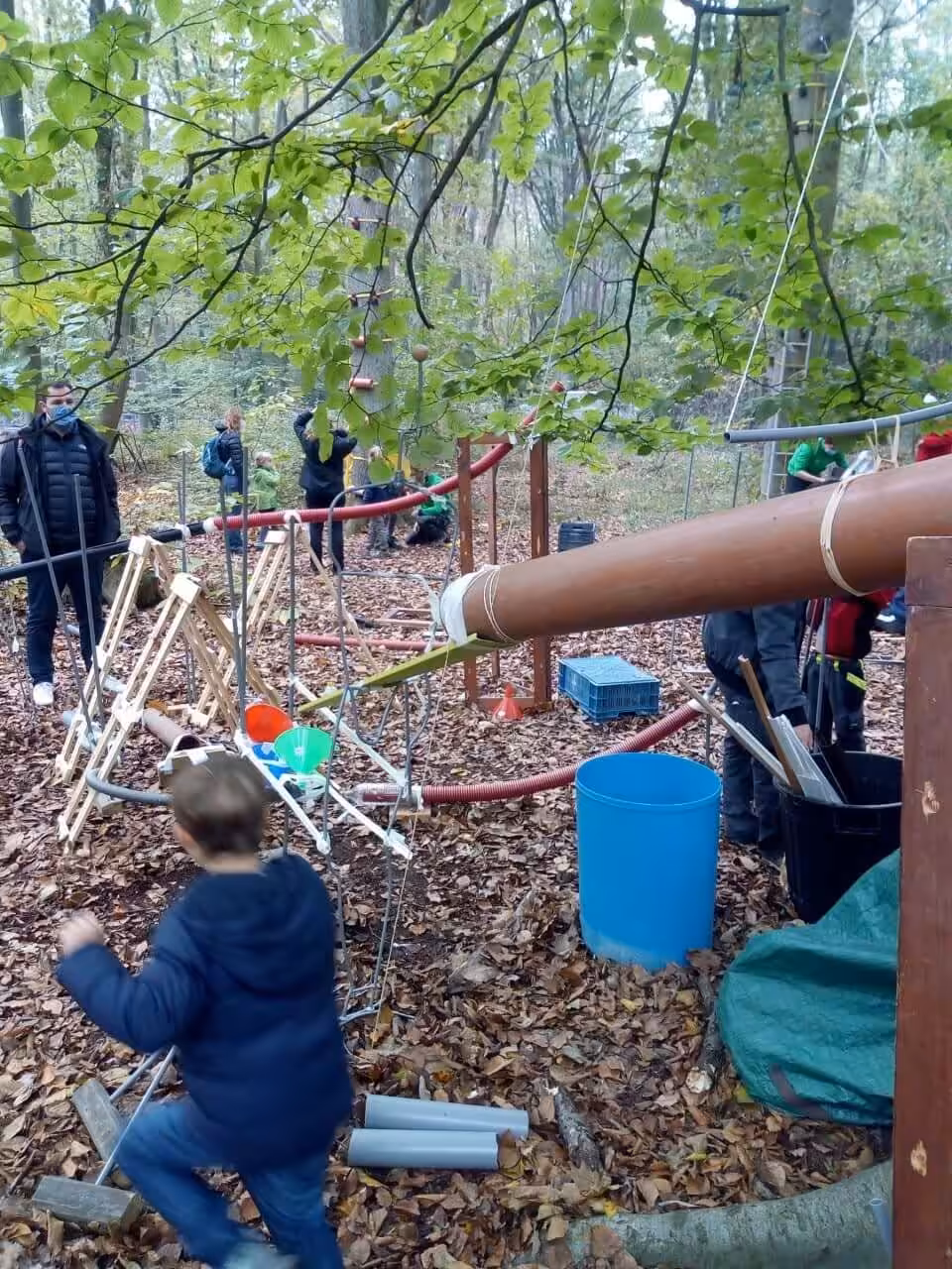 Kinderen spelen in bos met houten constructies.
