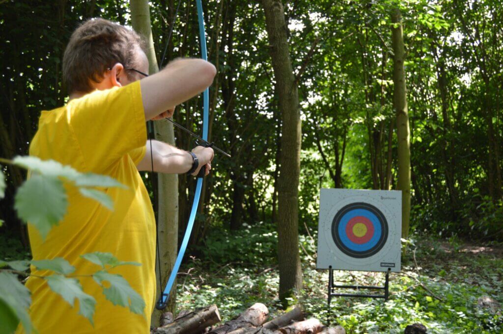 man met gele shirt mikt op doel met boog