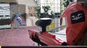 Paintball speler met rood geweer richt op tegenstander.