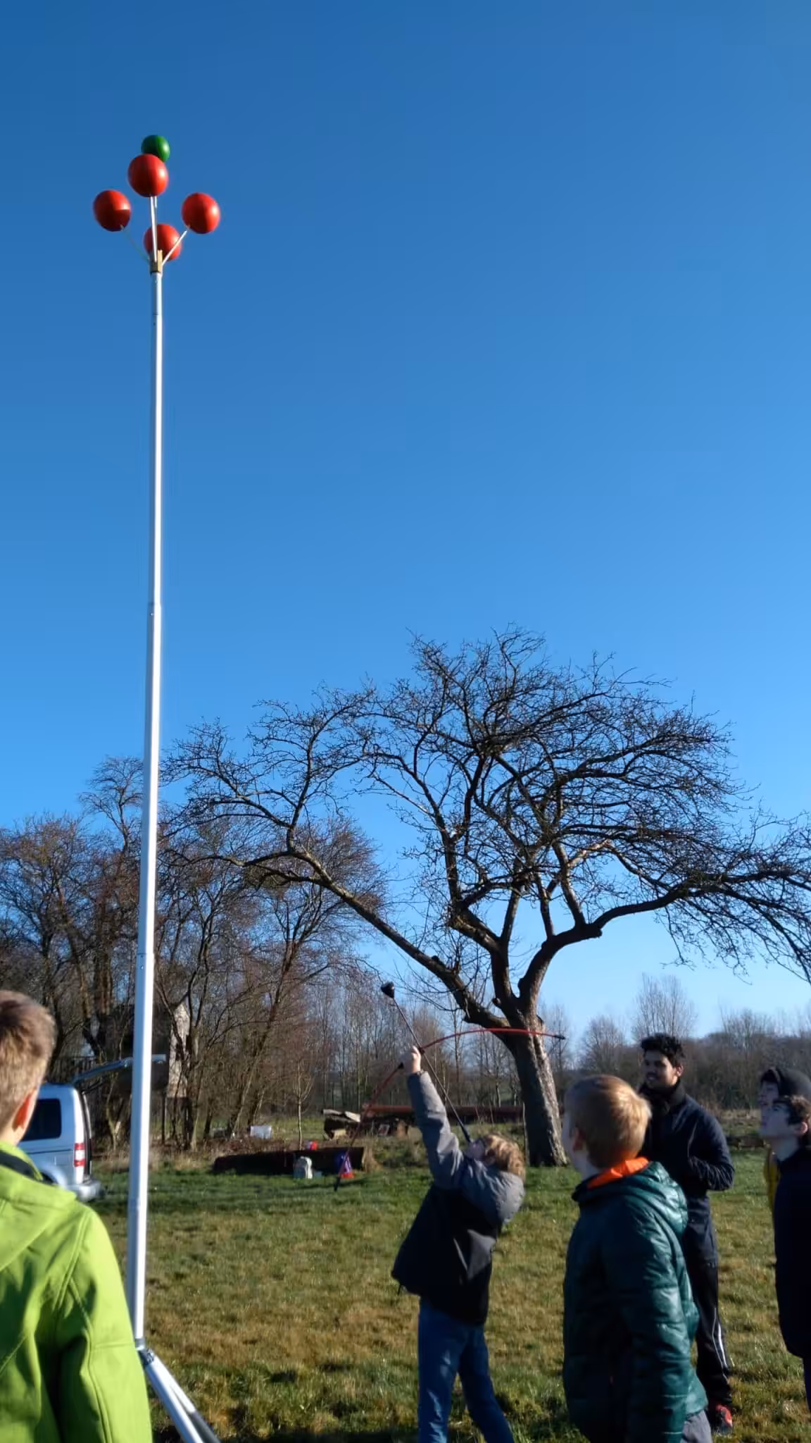 Kinderen kijken naar hoge paal met ballen.
