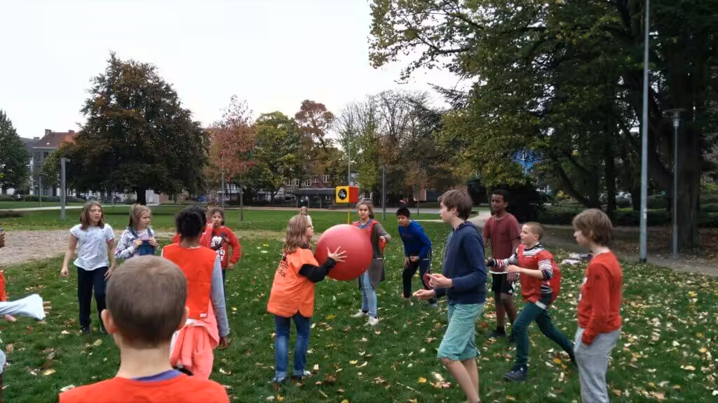 Kinderen spelen met rode bal in park.