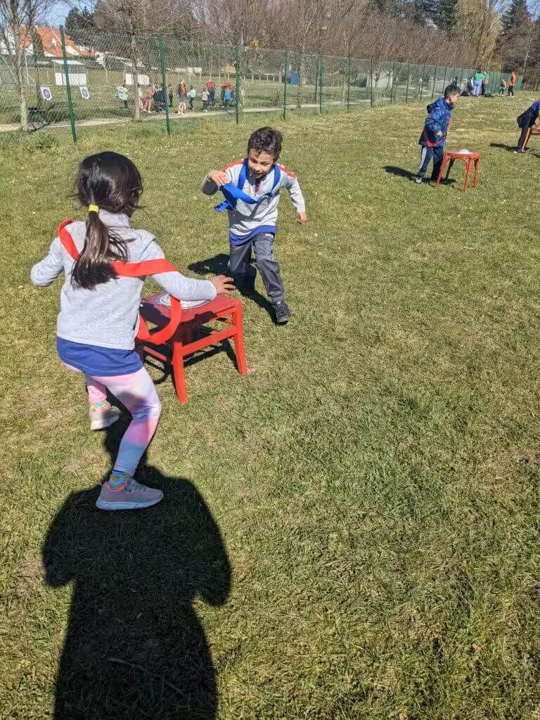 Kinderen spelen buiten met speelgoedtafels op grasveld.