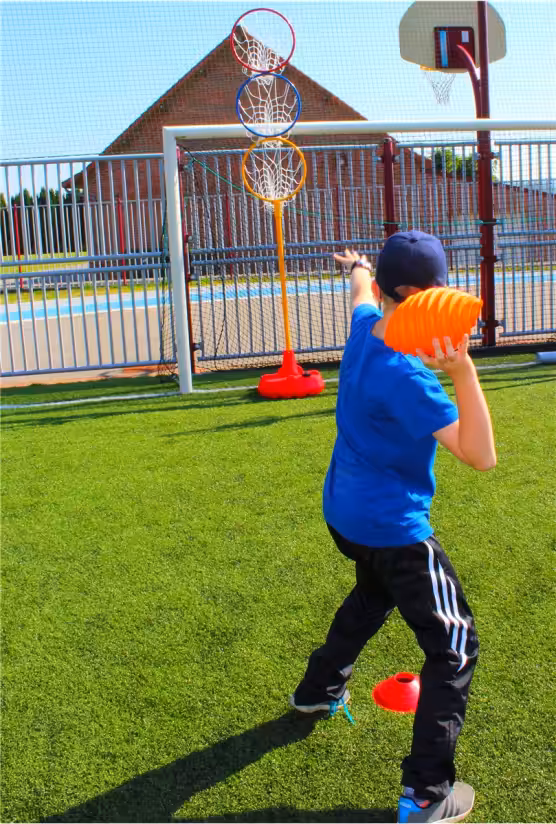 Kind gooit bal op kleurrijke basketbalringen buiten.